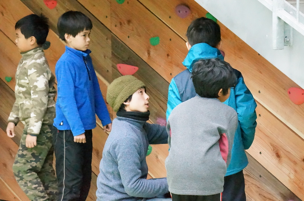 An adult and kids are looking at the bouldering wall